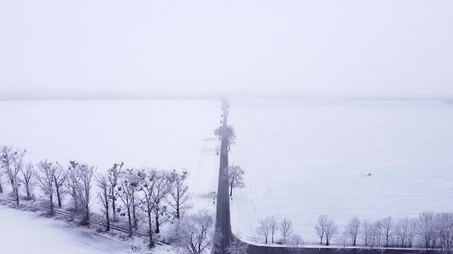 Rural crossroads between snow-covered fields and meadows on a sunless hazy morning. Aerial, flying forward.