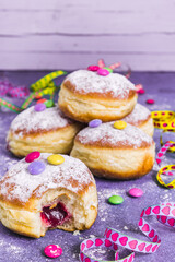 Krapfen, Berliner or donuts with streamers, confetti and chocolate beans. Colorful carnival or birthday image on purple background, vertical with copy space.