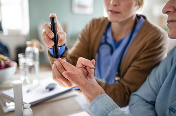 Midsection of caregiver or healthcare worker with senior woman patient, measuring blood glucose...