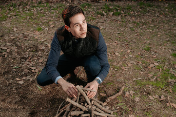 Portrait young man preparing pile of wood to turn on fire. Camping, natural lifestyle concept.