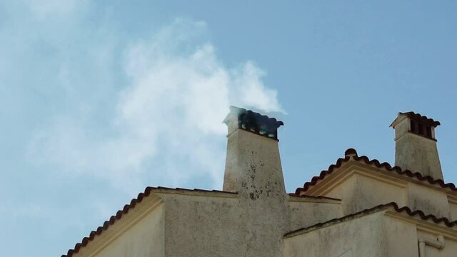 Smoke from the chimney of a picturesque old house in the village. Clear winter day. Mediterranean white house against the blue sky. Fireplace. Smoke from the kitchen. White walls and a tiled roof.