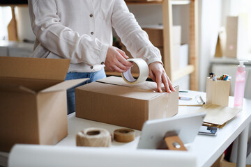 Unrecognizable woman dropshipper working at home, packing parcels. Coronavirus concept.