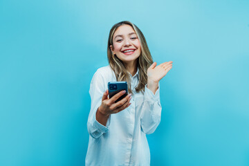 Happy and smiling attractive girl on a blue background holds a phone in his hand and joyfully looks at the camera. Commerce. Place for text