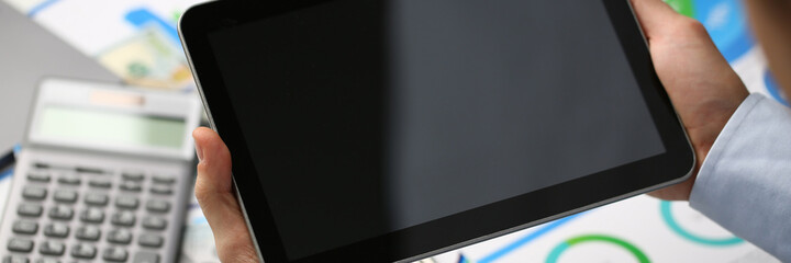 Top view of male financier working at the table and holding digital tablet with documents on the background. Finance and analytics concept