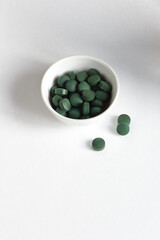 Green spirulina pills in a bowl on white background, minimalist composition with plant organic vegan food supplement and rainbow of light, closeup, healthy superfood concept