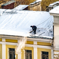 a worker cleans the roof of a house from snow in winter 