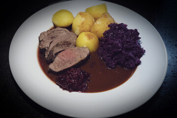 delicious meal from a young chamois buck with potatoes and red cabbage, brown sauce and cranberries on a white plate