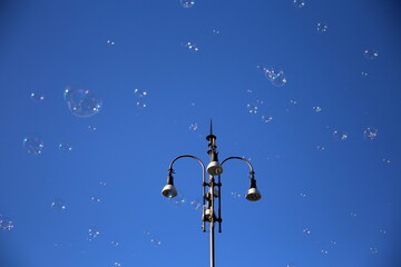 Obraz na płótnie Canvas Lamppost with the clear blue sky in the background, surrounded by soap bubbles