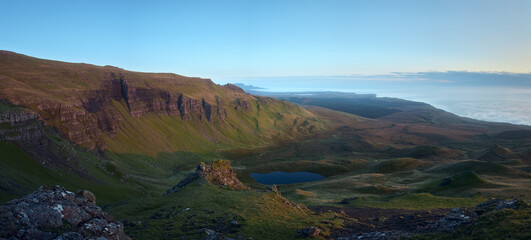Stunning view of a small lake with mountains and sea covered with low clouds before dawn. The Isle of Skye, Scotland, UK.