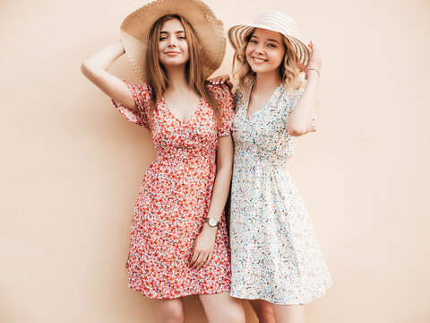 Two young beautiful smiling hipster female in trendy summer sundress.Sexy carefree women posing on the street near wall in hats. Positive models having fun and hugging