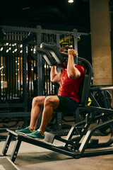 Athletic man doing legs exercise on squat machine at the gym