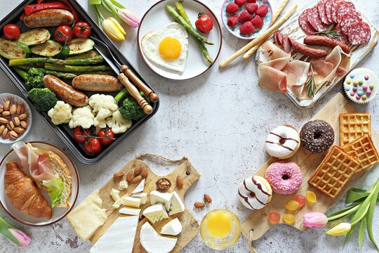 Breakfast food table. Festive brunch set, meal variety with grill platter, fried egg, croissant sandwich, cheese platter and desserts. Overhead view