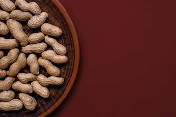 Unpeeled peanuts in a clay plate on a brown background