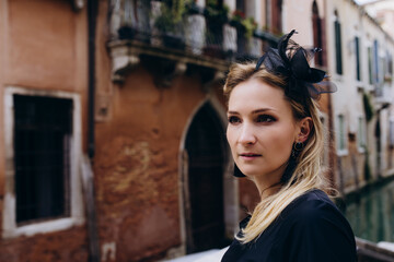 Fototapeta premium Facial portrait of a girl against the background of a narrow street. There is a black bow on the head.