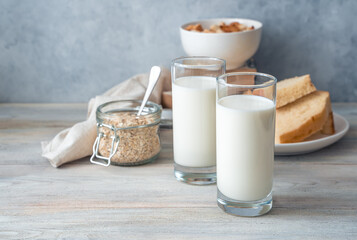 Milk in two glasses, bread and oatmeal on a gray background. Side view with copy space. The concept of useful products.