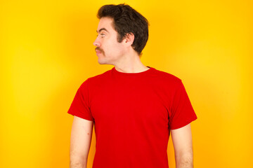 Fototapeta premium Close up side profile photo young Caucasian man wearing red t-shirt standing against yellow background not smiling attentive listen concentrated