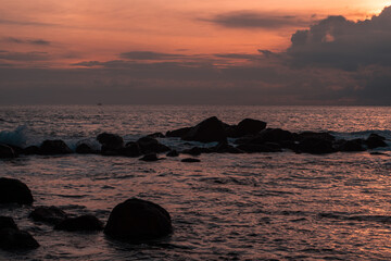 Krajobraz wybrzeża ze skałami nad oceanem z falami na tle pomarańczowego zachodzącego słońca. Piękne tropikalne tło.