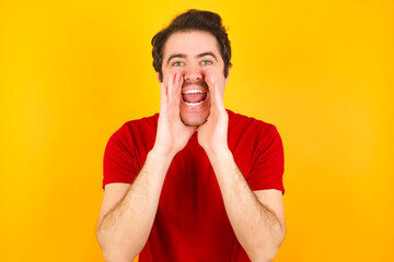 young Caucasian man wearing red t-shirt standing against yellow background shouting excited to front.