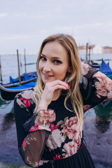 Fototapeta na wymiar Portrait of a cheerful girl on the background of blue gondolas. A tourist travels around Venice.