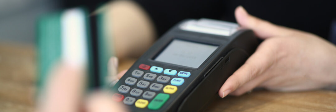 Close up of bartender with payment terminal and client hand with credit card. Modern technology and people concept