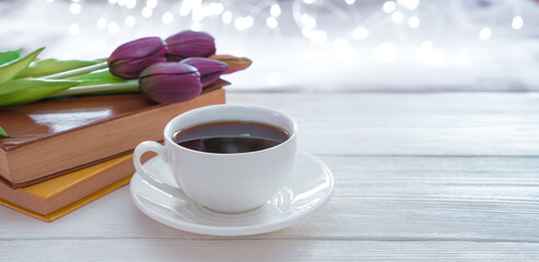 Coffee, books and flowers on a light background with glowing garlands. Side view with copy space, panorama. The concept of holidays.