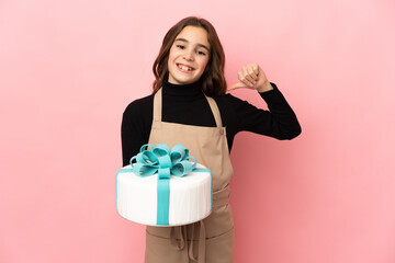 Little Pastry chef holding a big cake isolated on pink background proud and self-satisfied