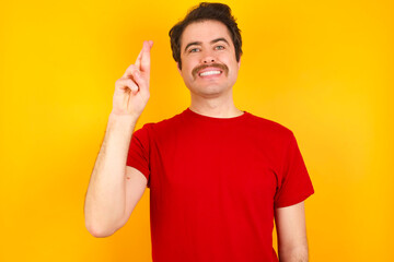Fototapeta premium Young Caucasian man wearing red t-shirt standing against yellow background pointing up with fingers number ten in Chinese sign language Shi