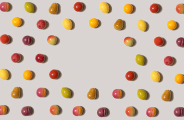 Flat lay isometric pattern of small marzipan fruit shaped candies in different colors and shapes - lemon, lime, pear, peach, plum, orange, apple against light gay background. Centrally copy space.