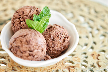 Chocolate ice cream with mint leafe. three balls in a white bowl on a vintage table.