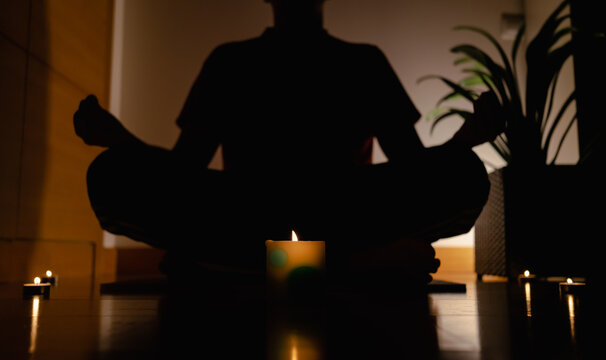 Relaxed Person Sitting On The Yoga Mat With Legs Crossed And Meditating With Candles