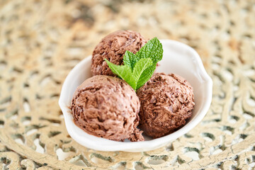 Chocolate ice cream with mint leafe. three balls in a white bowl on a vintage table.