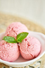 Strawberry ice cream with mint leaf. three balls in a white bowl on a vintage table. sorbet