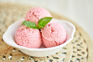 Strawberry ice cream with mint leaf. three balls in a white bowl on a vintage table. sorbet