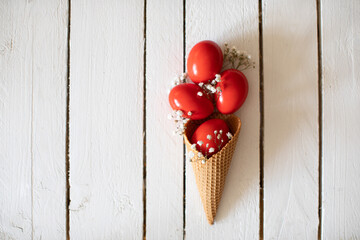 Red Easter eggs in an ice cream cone on a white wooden background. Creative minimal concept.