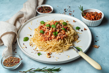 Spaghetti with bolognese pasta seasoned with basil, nuts and cheese on a gray background. Side view, horizontal orientation with space to copy. Culinary background.