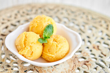 Mango ice cream with mint leaf. three balls in a white bowl on a vintage table. sorbet