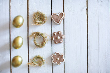 Easter eggs  gold colored, nests and decorative cakes on white wooden background with lot of copy space.