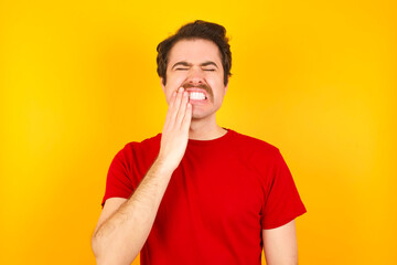 Fototapeta na wymiar Young Caucasian man wearing red t-shirt standing against yellow background touching mouth with hand with painful expression because of toothache or dental illness on teeth.