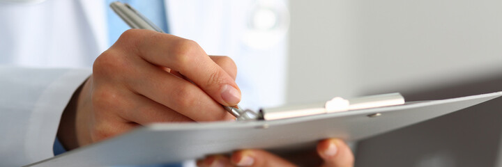 Close up of female doctor in a white medical coat holding questionnaire and writing information...