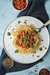 Pasta bolognese with basil and nuts in a flat plate on a dark napkin on a gray background. The view from the top. The concept of a culinary background.