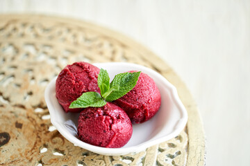 Berry ice cream with mint leaf. three balls in a white bowl on a vintage table. sorbet