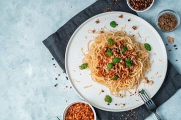 Culinary background with bolognese pasta, basil, cheese and nuts on a dark napkin on a gray background. Top view, horizontal orientation with space to copy.