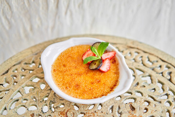 Classic creme brulee in glass bowl. Appetizing ice cream close up. Delicious dessert with grape and strawberry Sugary meal with caramel, mint and berries decoration. Restaurant sweet food