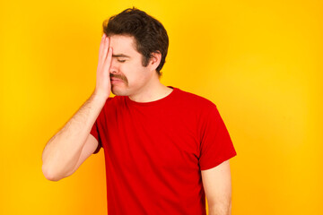 Obraz premium A very upset and lonely Young Caucasian man wearing red t-shirt standing against yellow wall crying,