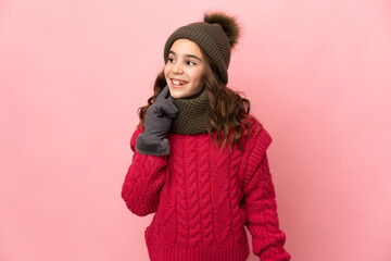 Little girl with winter hat isolated on pink background thinking an idea while looking up
