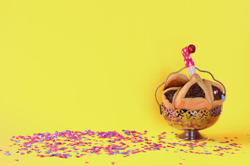 Purim holiday concept with hamantaschen cookies or hamans ears or oznei haman in hebrew, and noisemaker over joy yellow color with colorful confetti background.