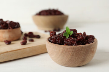Tasty dried cranberries and leaves in bowl on white table. Space for text