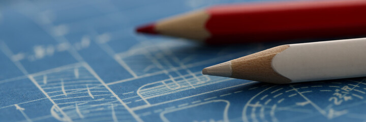 White and red pencils lying on blueprint closeup background. Project documentation concept