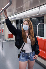 A beautiful white Latina woman using the city subway leaning on a support with her right hand wearing a mask for the coronavirus pandemic in an American plane