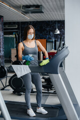 Fototapeta na wymiar The girl in the mask disinfecting the gym equipment during a pandemic.